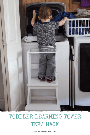 little kid standing in a learning tower at a washing machine getting cloths out of a laundry basket