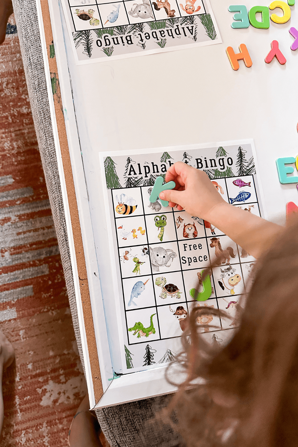 Alphabet bingo, a bingo board with a bunch of different animals. A hand placing a magnetic letter K on the board.