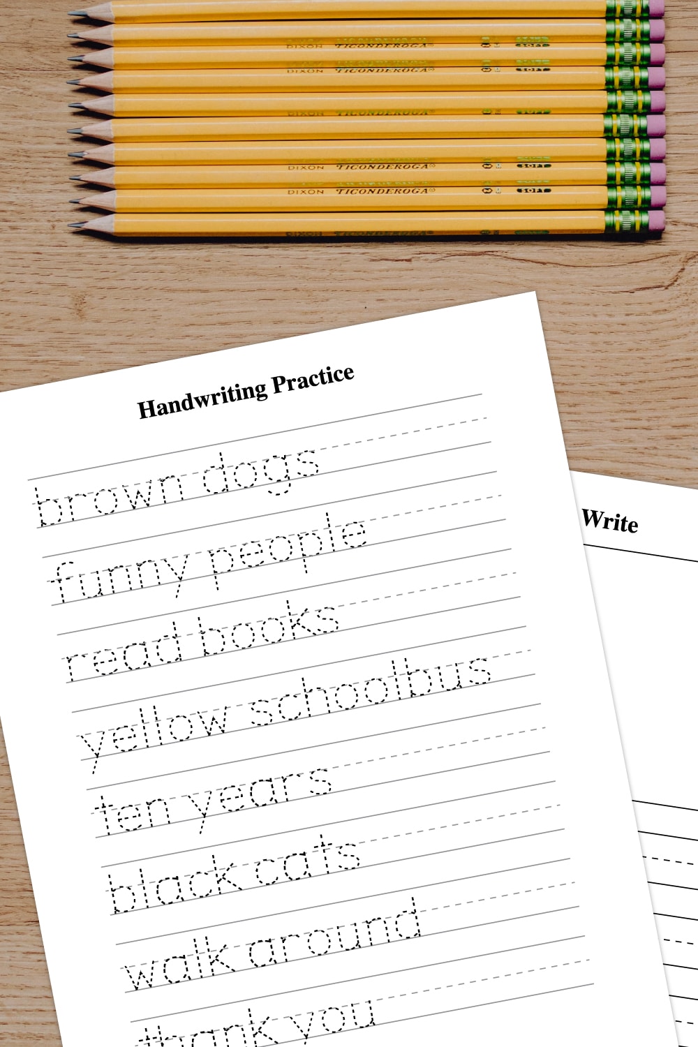 Wooden background with top view of yellow pencils stacked and preview of handwriting practice worksheets on the bottom. 