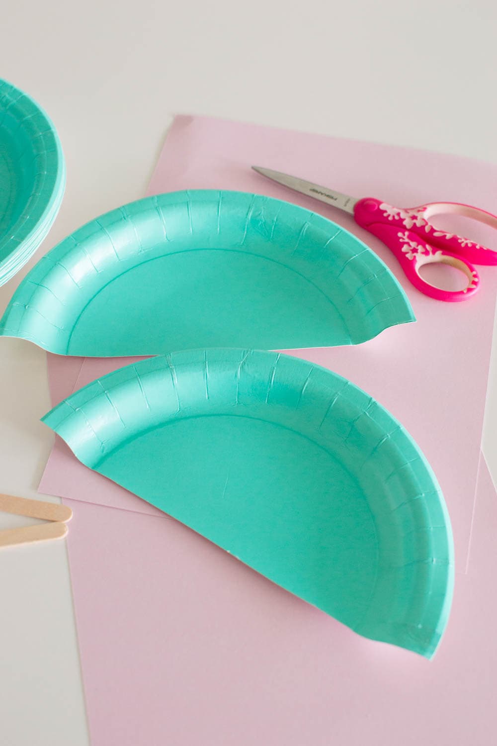 A teal paper plate cut in half with scissors and other craft supplies in the background