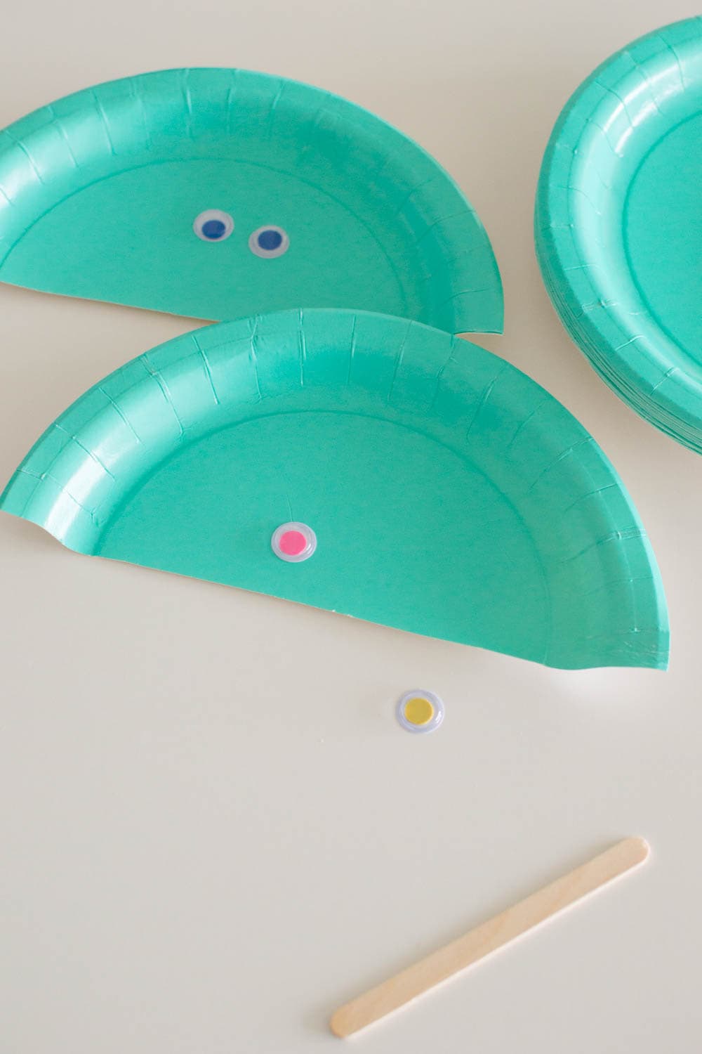 Adding colorful googly eyes to paper plate halves