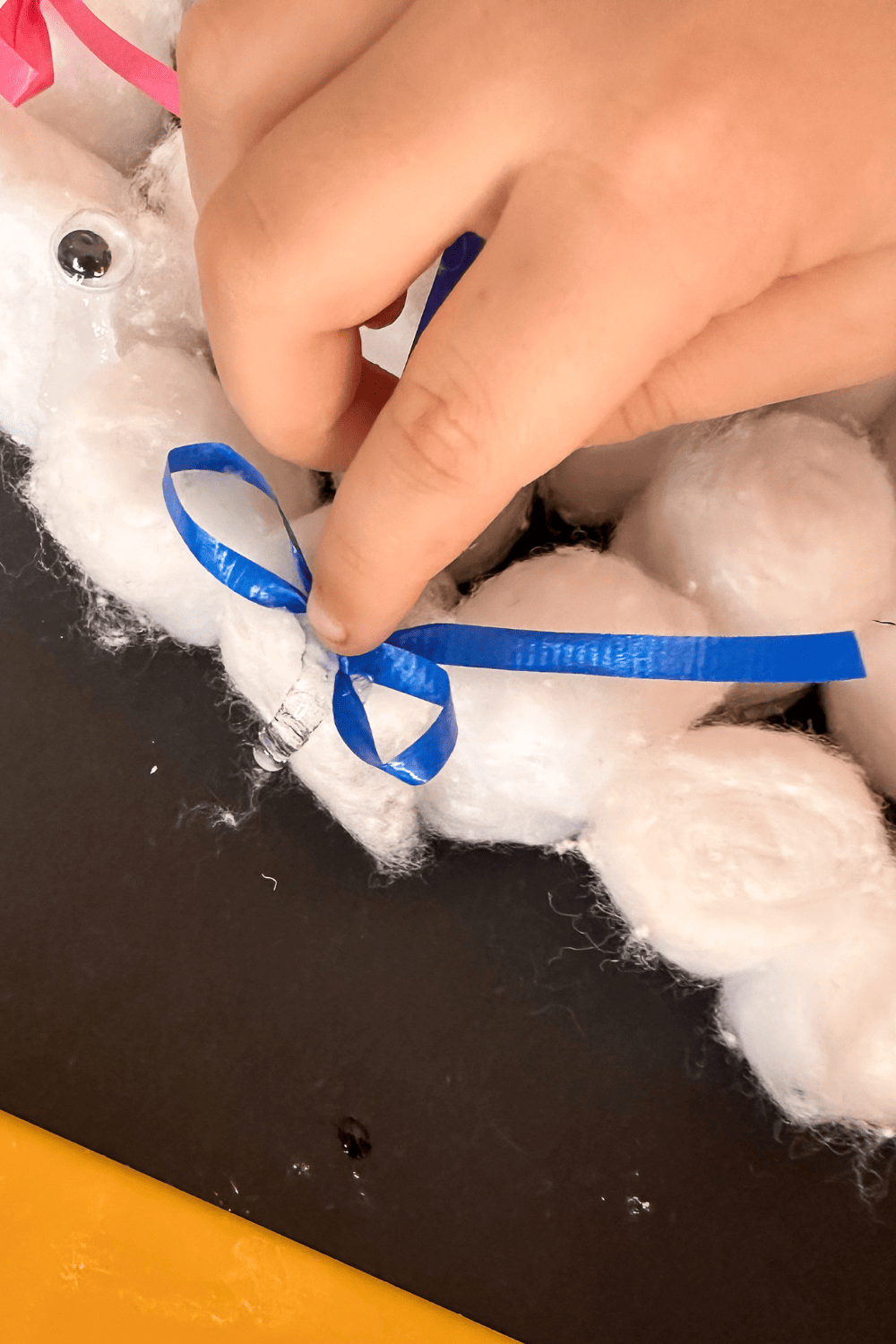 a child's hand placing a blue bow on cotton balls