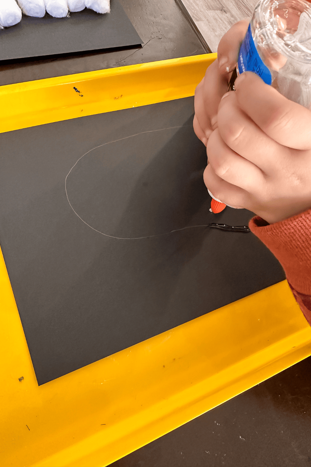 a child's hands applying glue to black paper