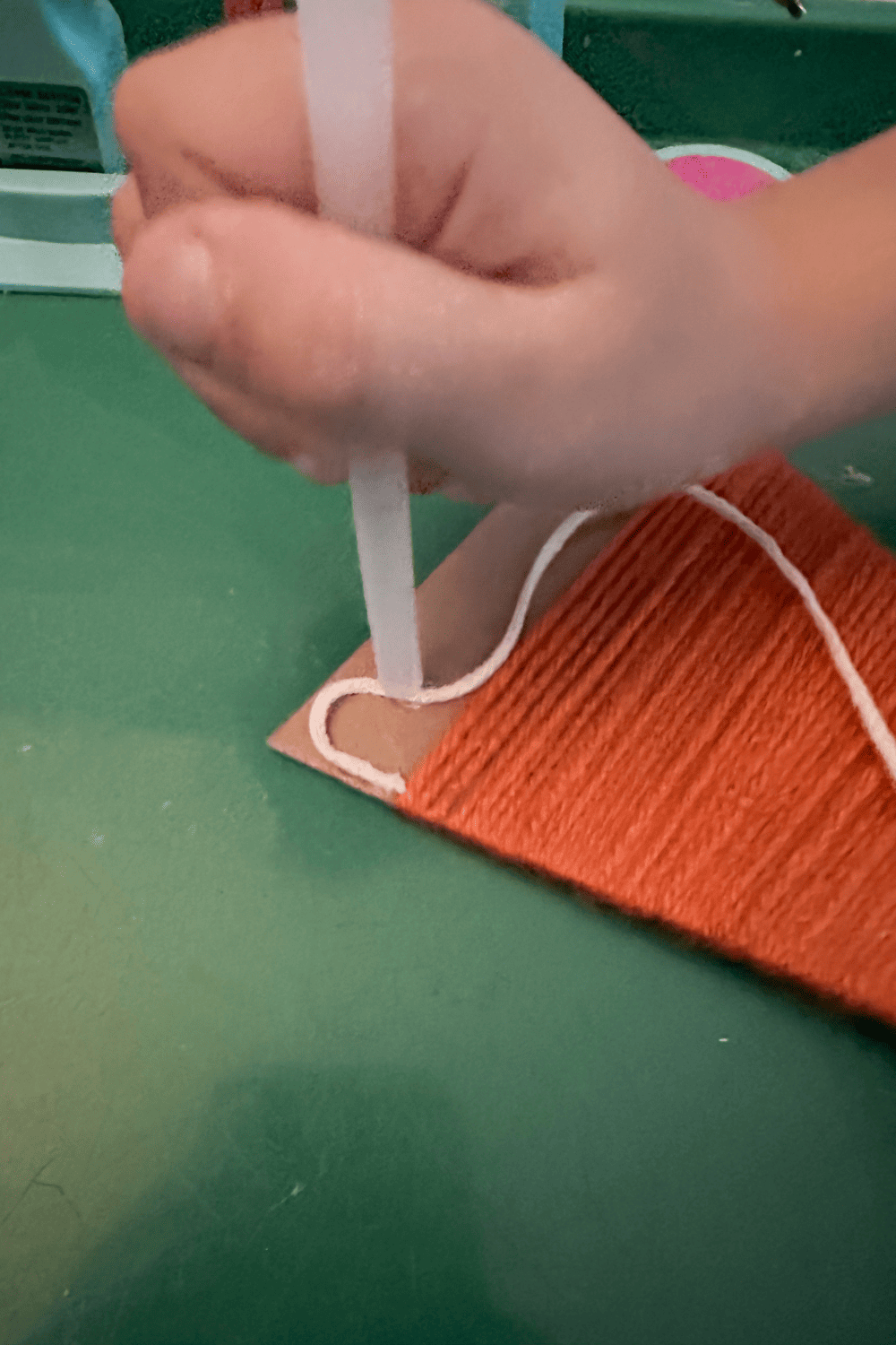 child using hot glue stick to help attach yarn to cardboard