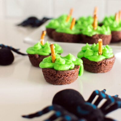 Witch cauldron brownies with green frosting and a pretzel stir stick.