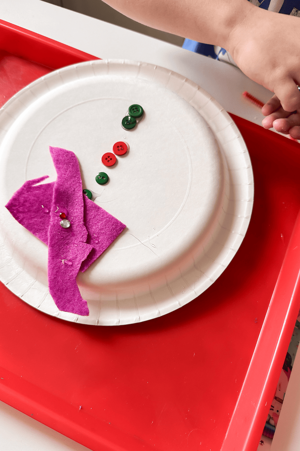 Buttons and felt and gems being used to decorate a paper plate snowman