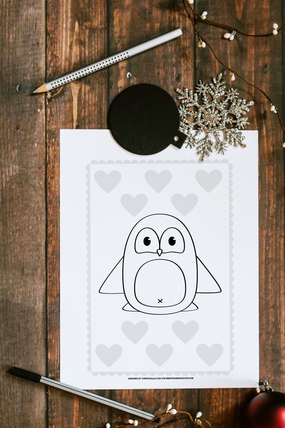 Preview of a penguin coloring page on wooden plank table with pencil, marker and various winter decor on top and bottom.