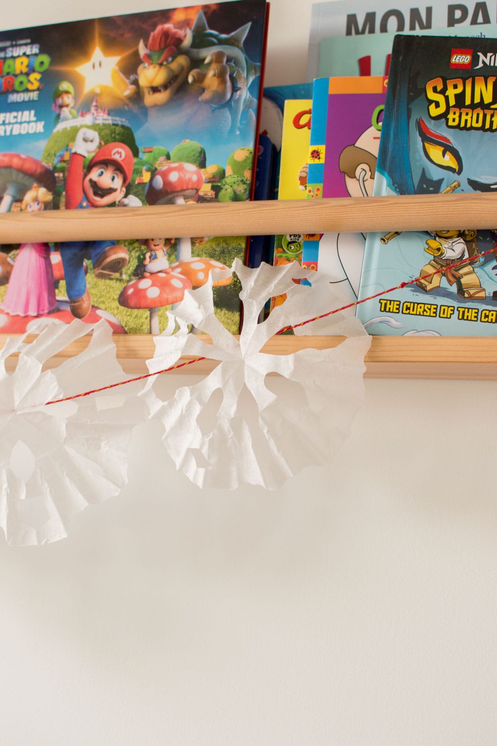 A garland made up of red string and coffee filter snowflakes hanging off a wall bookshelf