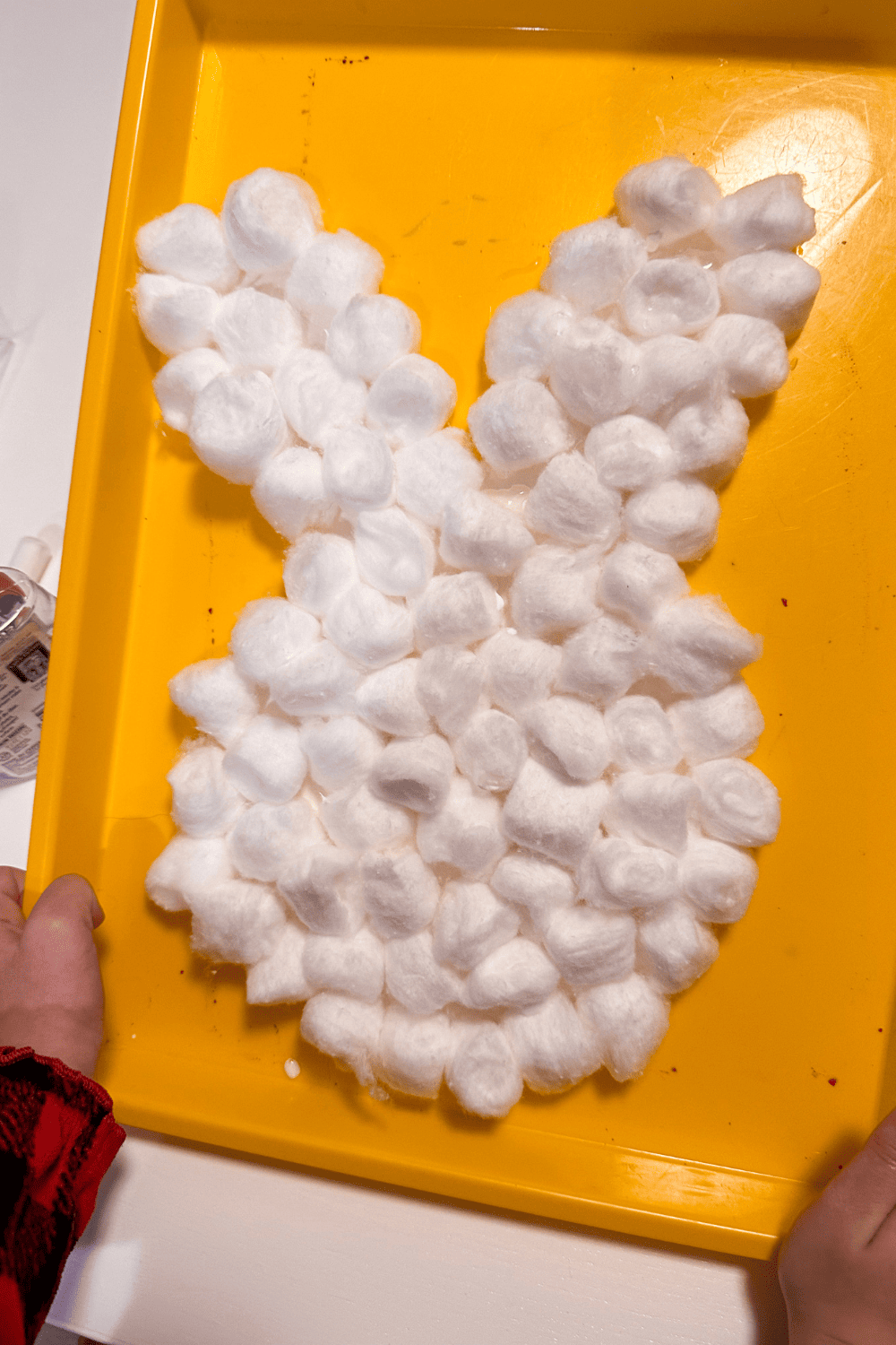 Cotton ball bunny on a tray with small hands holding the sides