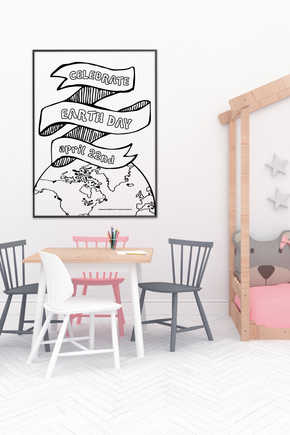 Preview of celebrate earth day illustration in a poster frame on white wall in kids room with desk and chairs under and view of bed with bear cushion on the right side. 