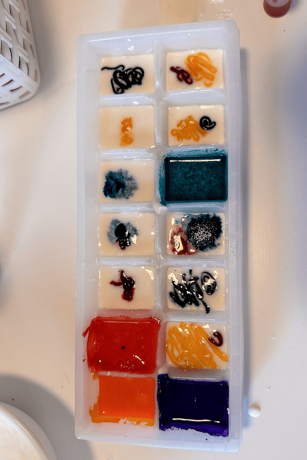Homemade watercolor paints in a ice cube tray, base of the paint is white and get food coloring has been put on top. A few have been mixed in.