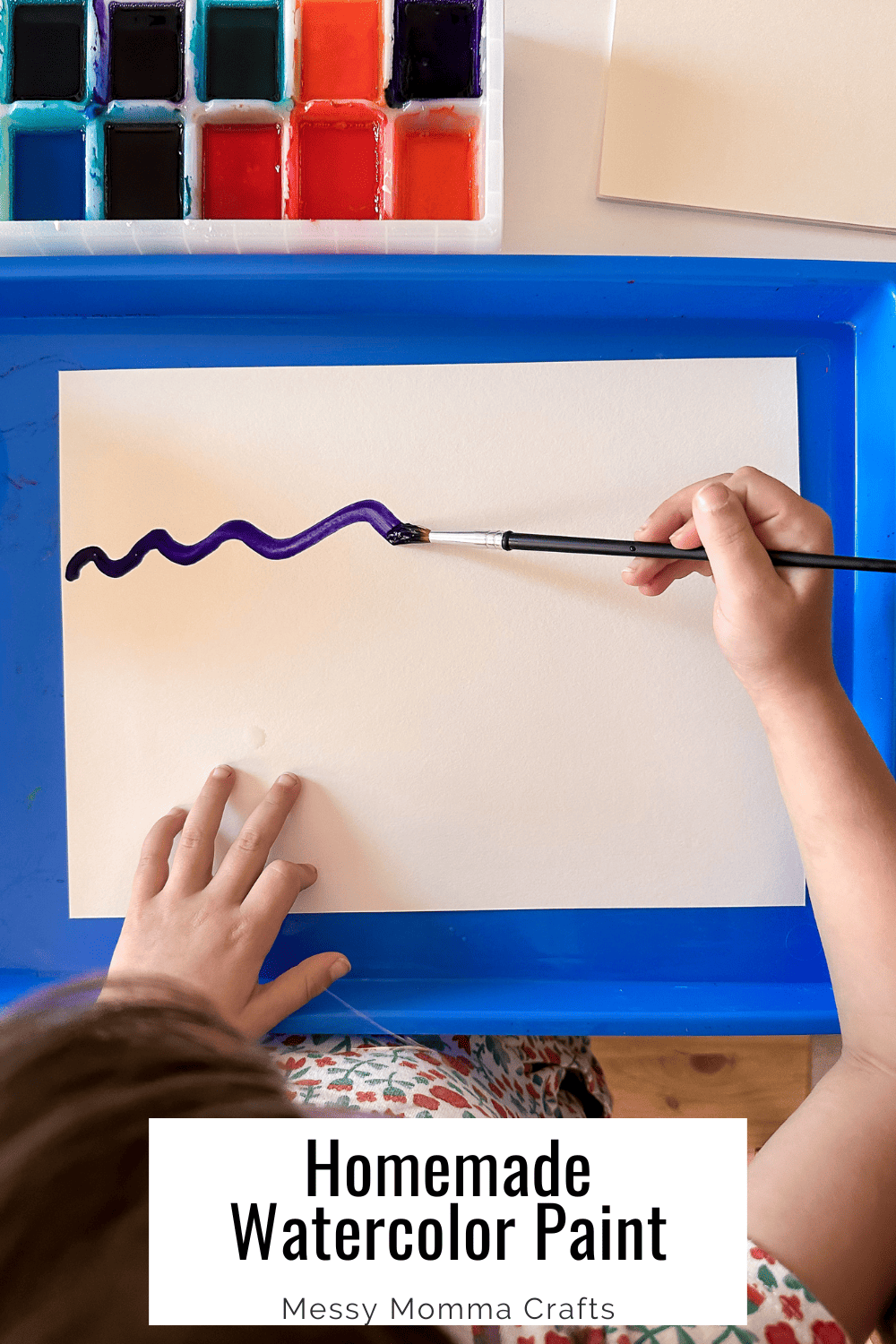 Child painting with homemade watercolor paints in a purple color. Homemade watercolor paints in an ice cube tray in the top left of the photo.