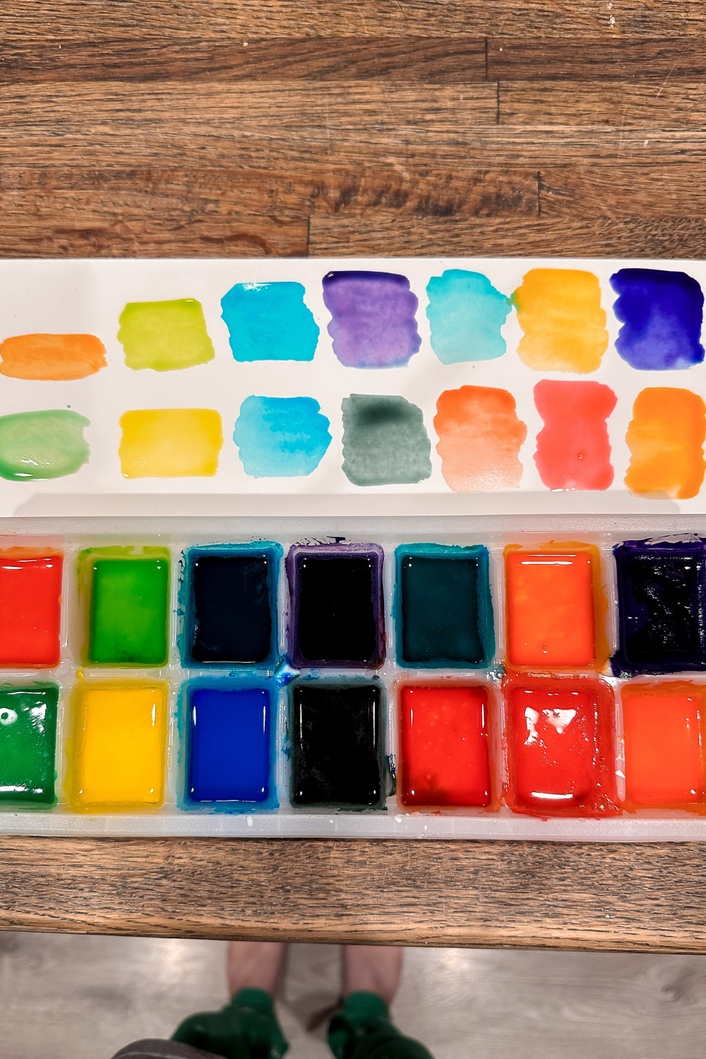 Homemade watercolor paints in a ice cube tray. Paints are swatched above the tray and the swatches are wet.