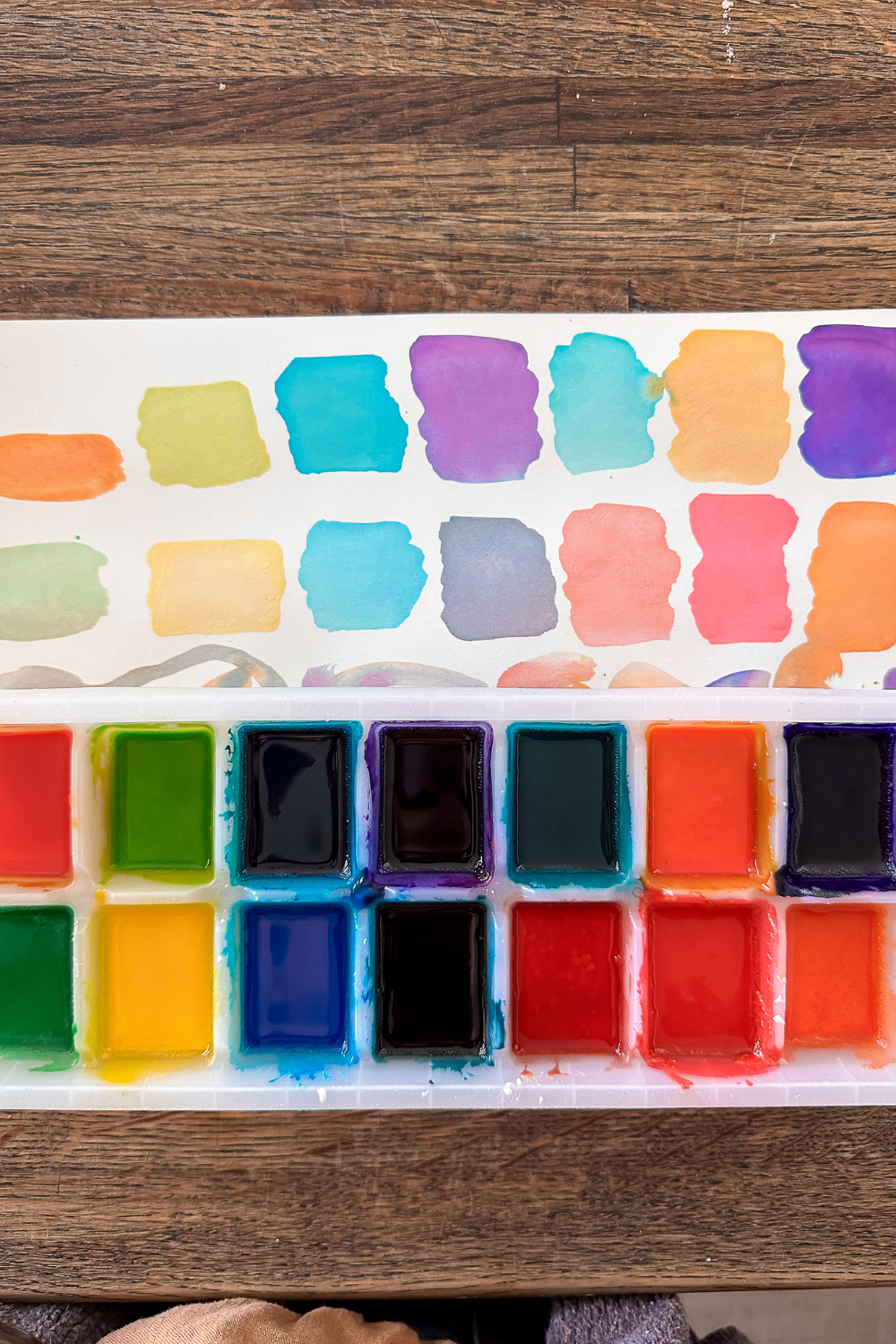 Homemade watercolor paints in a ice cube tray. Paints are swatched above the tray and the swatches are dry.
